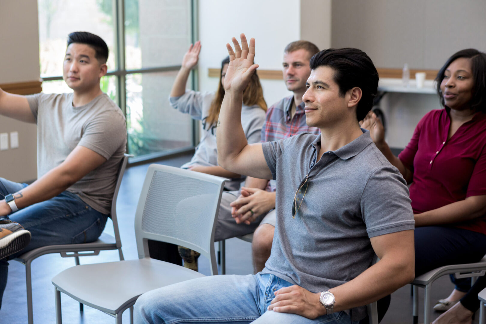 Attentive group of male and female veterans raise their hands in response to a question during a meeting for veterans.