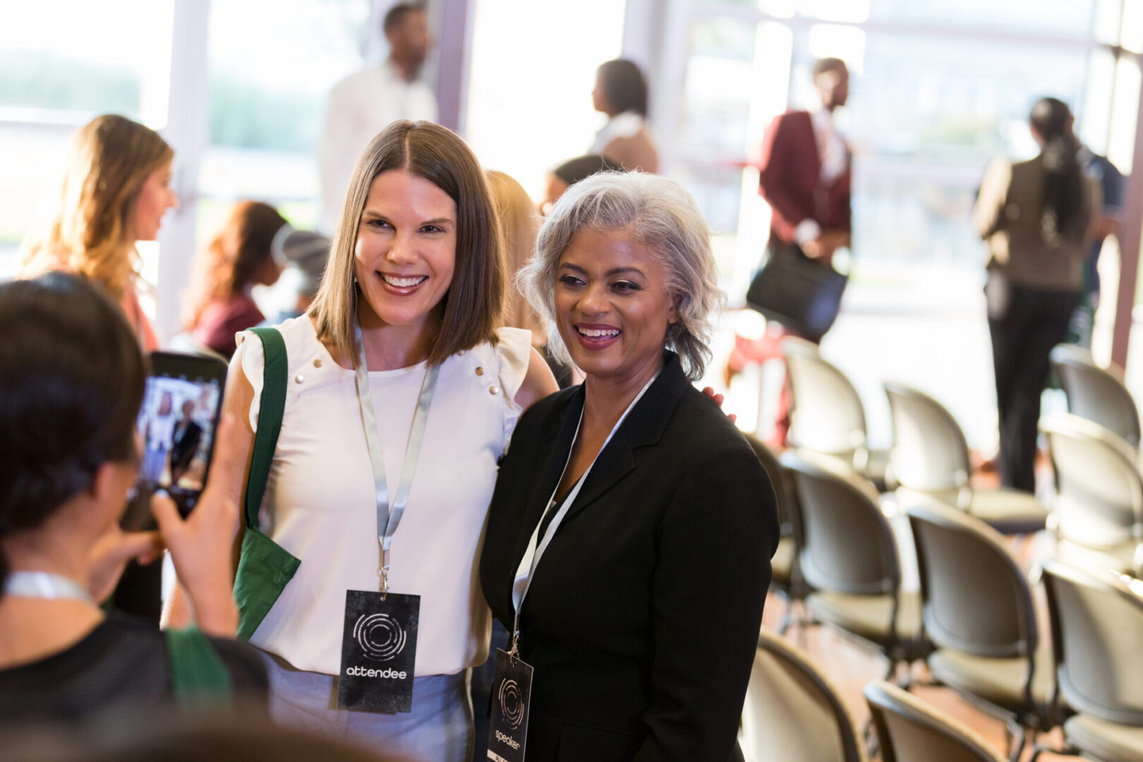Confident mature African American female conference speaker smiles while posing for a photo with a female conference attendee.