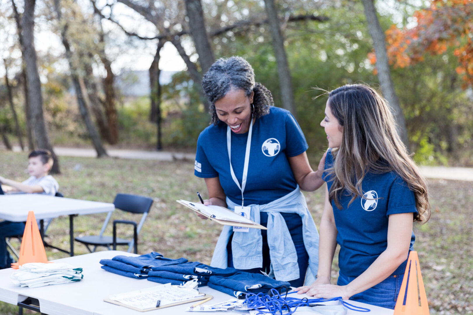 Women organize community cleanup event. They discuss something on a clipboard while standing at the event registration table.