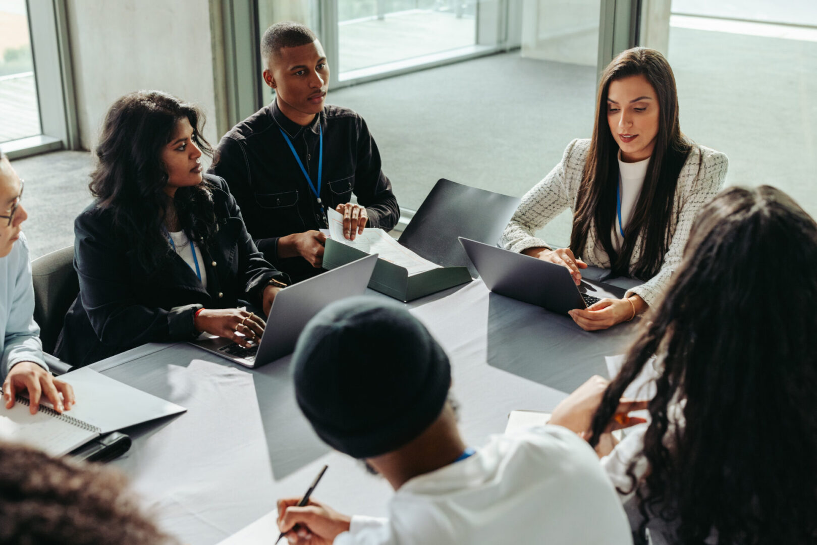 Diverse group of business people collaborating in an office setting. They engage in teamwork and discussion, working together on laptops.
