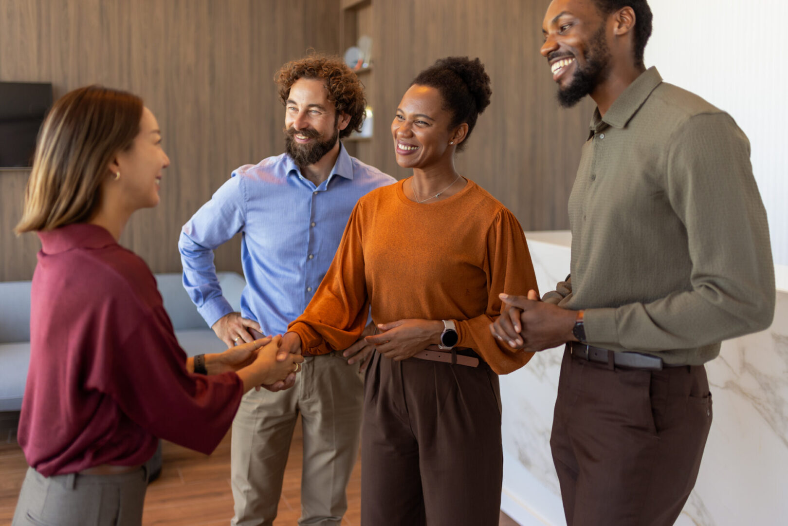 Two women and two men engage in friendly, confident handshakes during a casual meeting in a sunlit, contemporary office. Great for networking, onboarding, or client welcome imagery.