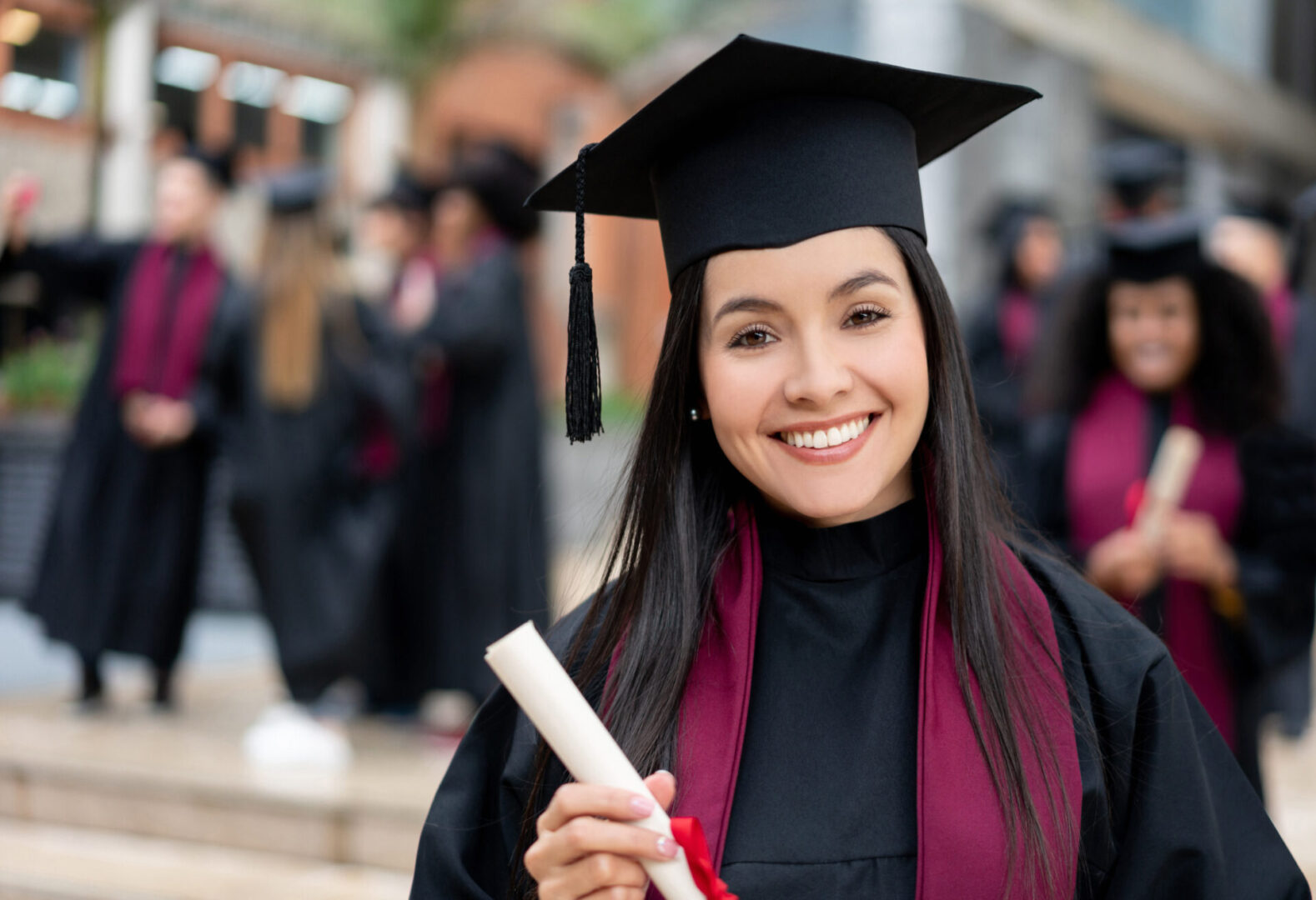 Portrait of a happy graduating student holding her diploma and looking at the camera smiling