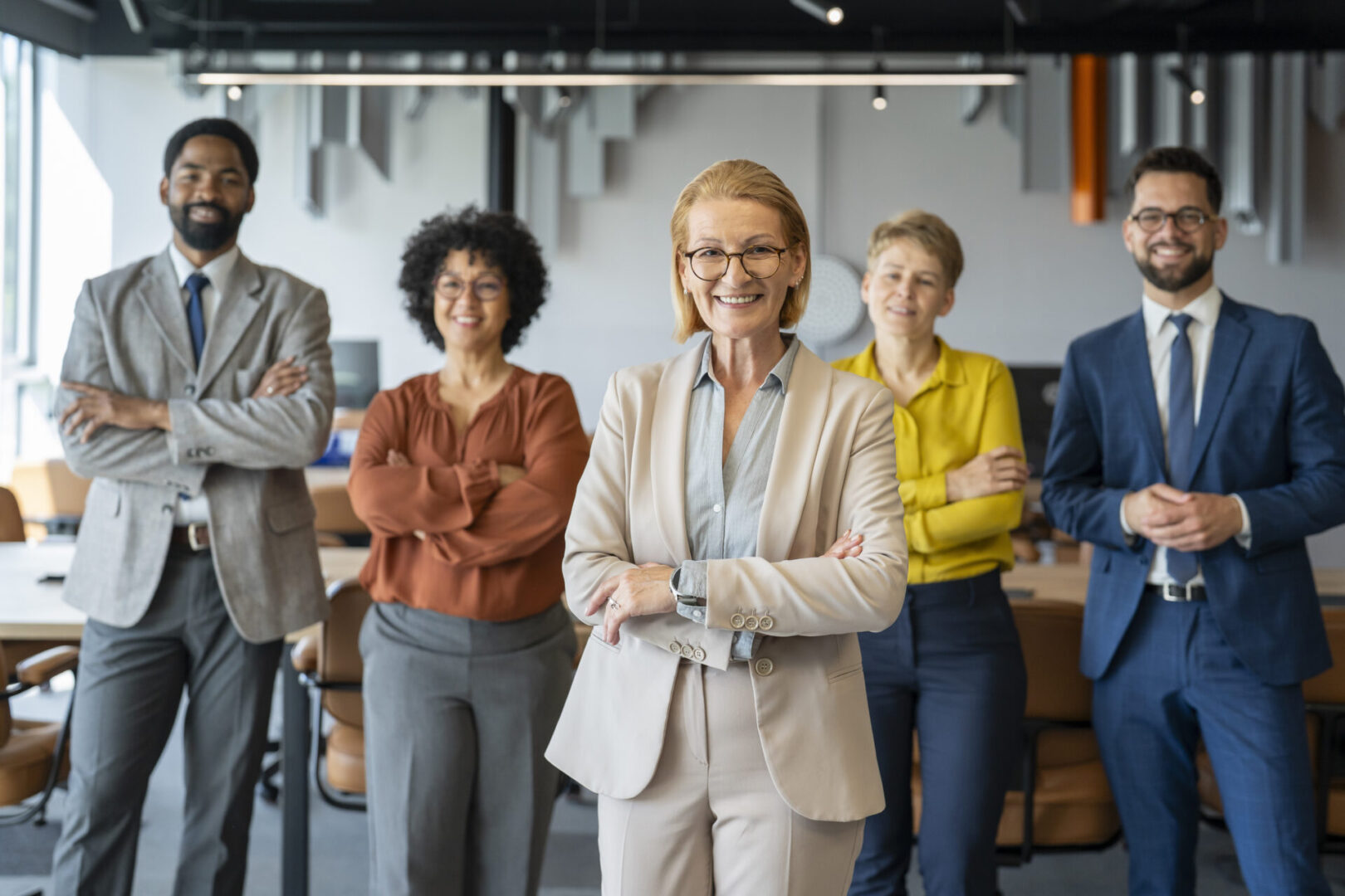 Diverse group of businesspeople standing together in their modern office with arms crossed, smiling at the camera