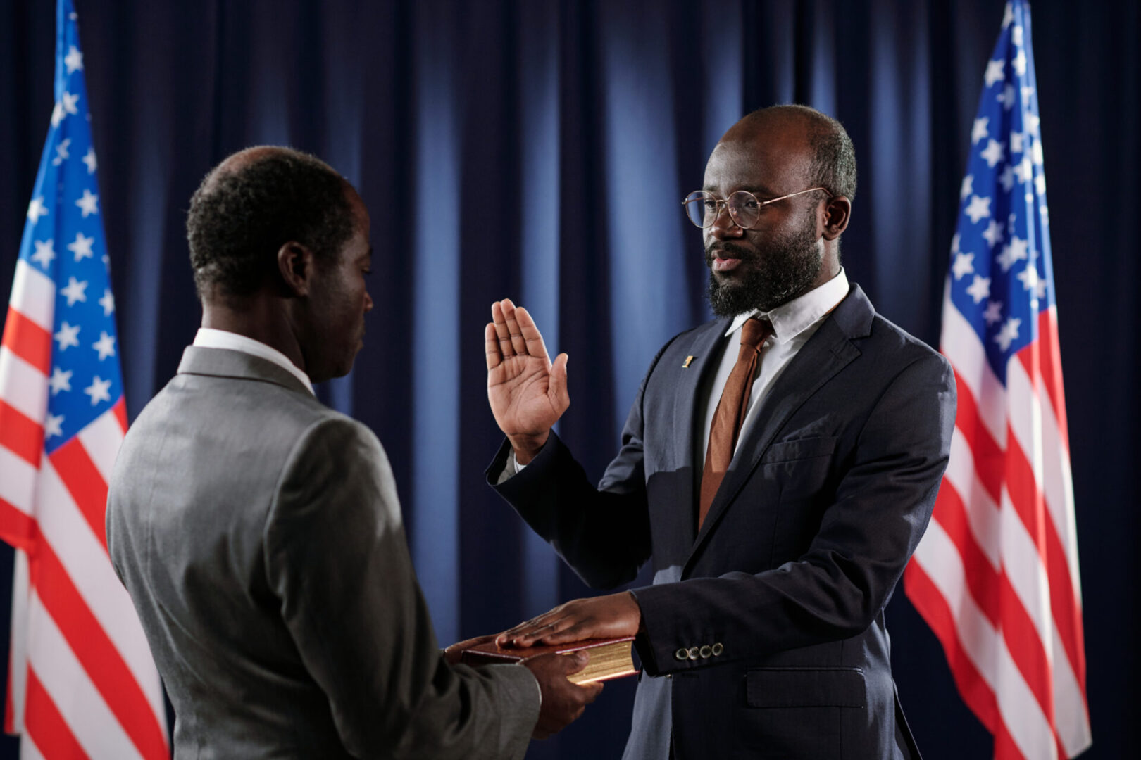 Young confident president of United States giving oath of office during inauguration ceremony with open palm and left hand on Holy Bible
