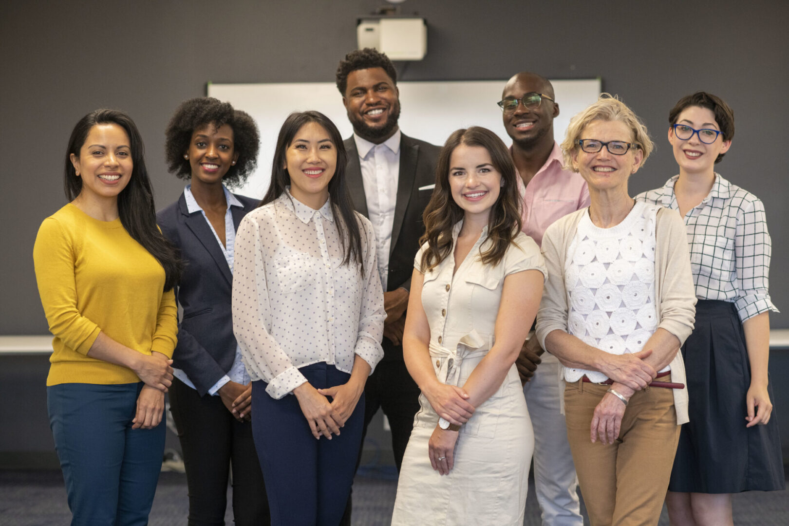 A  diverse group of colleagues pose together for a team photo. They are all looking directly at the camera and smiling. They are wearing formal business clothes.